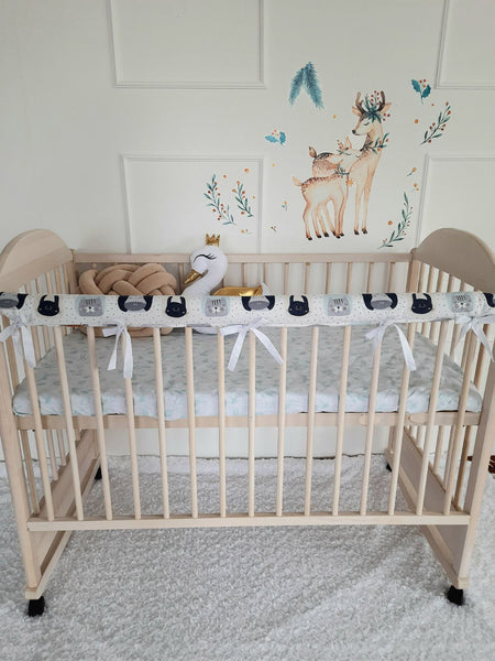 Baby crib adorned with a soft light pink rail cover, a protective white braided bumper, playful star-shaped pillows, and an elegant swan pillow, creating a charming and serene nursery atmosphere.