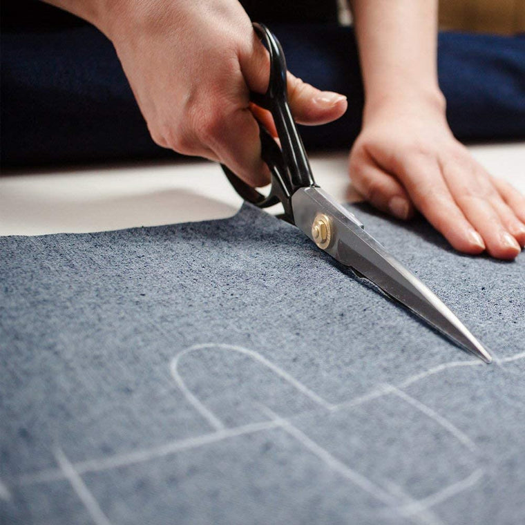 Person carefully cuts a piece of fabric with sharp scissors on a well-lit table