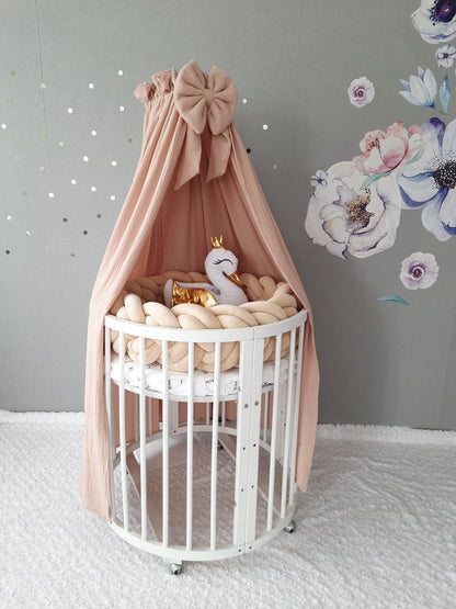 Muslin canopy in beige color over the crib. Double braided cot bumper and swan pillow on the crib