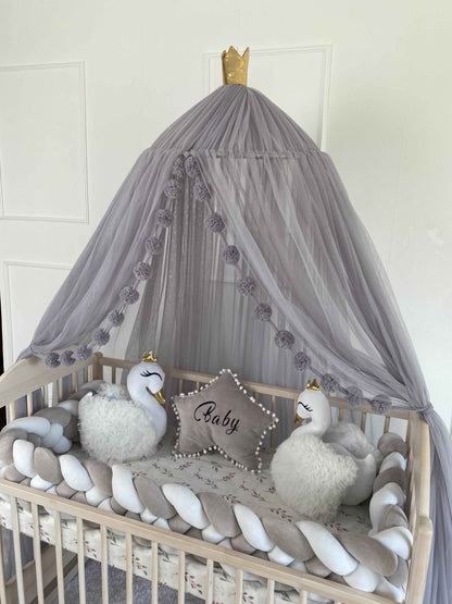 A baby crib with light gray canopy, featuring braided bumper and 2 white swan pillows and star pillow in light gray color