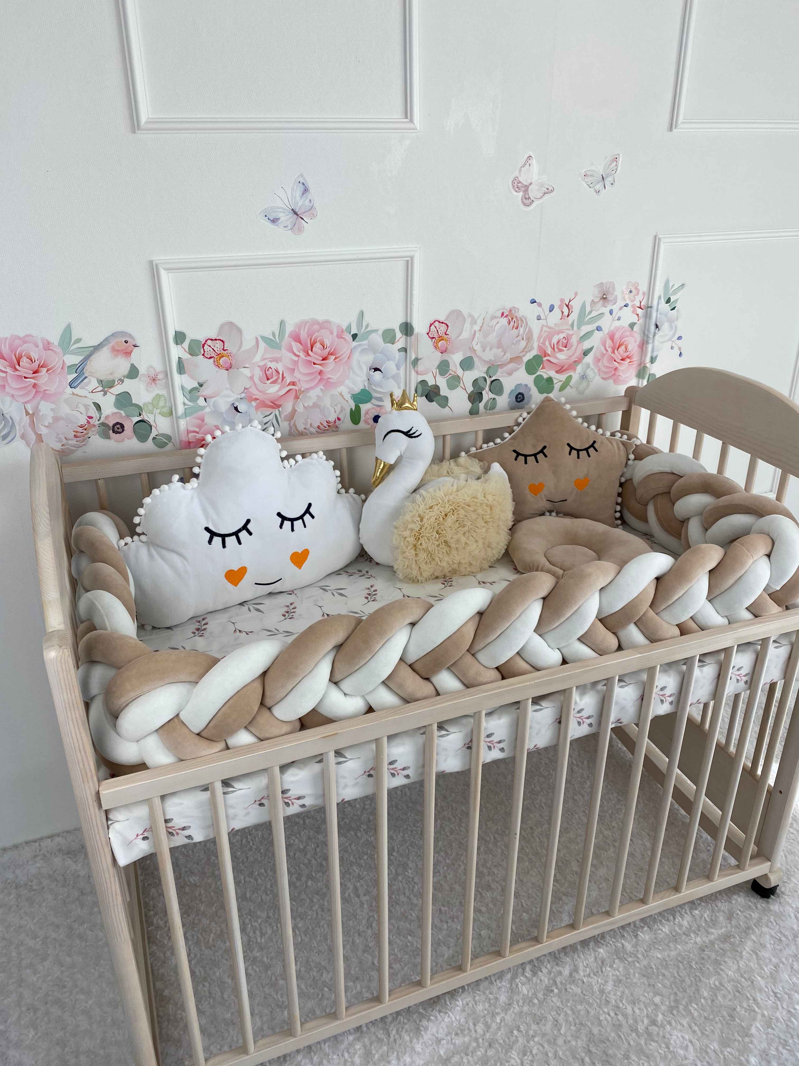 Baby set on the crib. Plush pillows and braided bumper