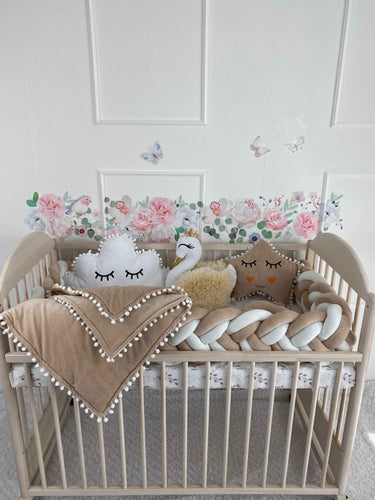 Cot bumper, 3 plush pillows and blanket on the crib. Cream and white colors. Front side.