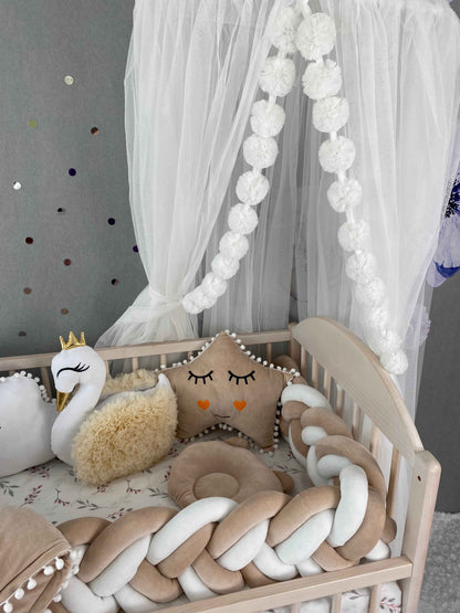 Cot bumper and pillows on the crib againg white canopy. 