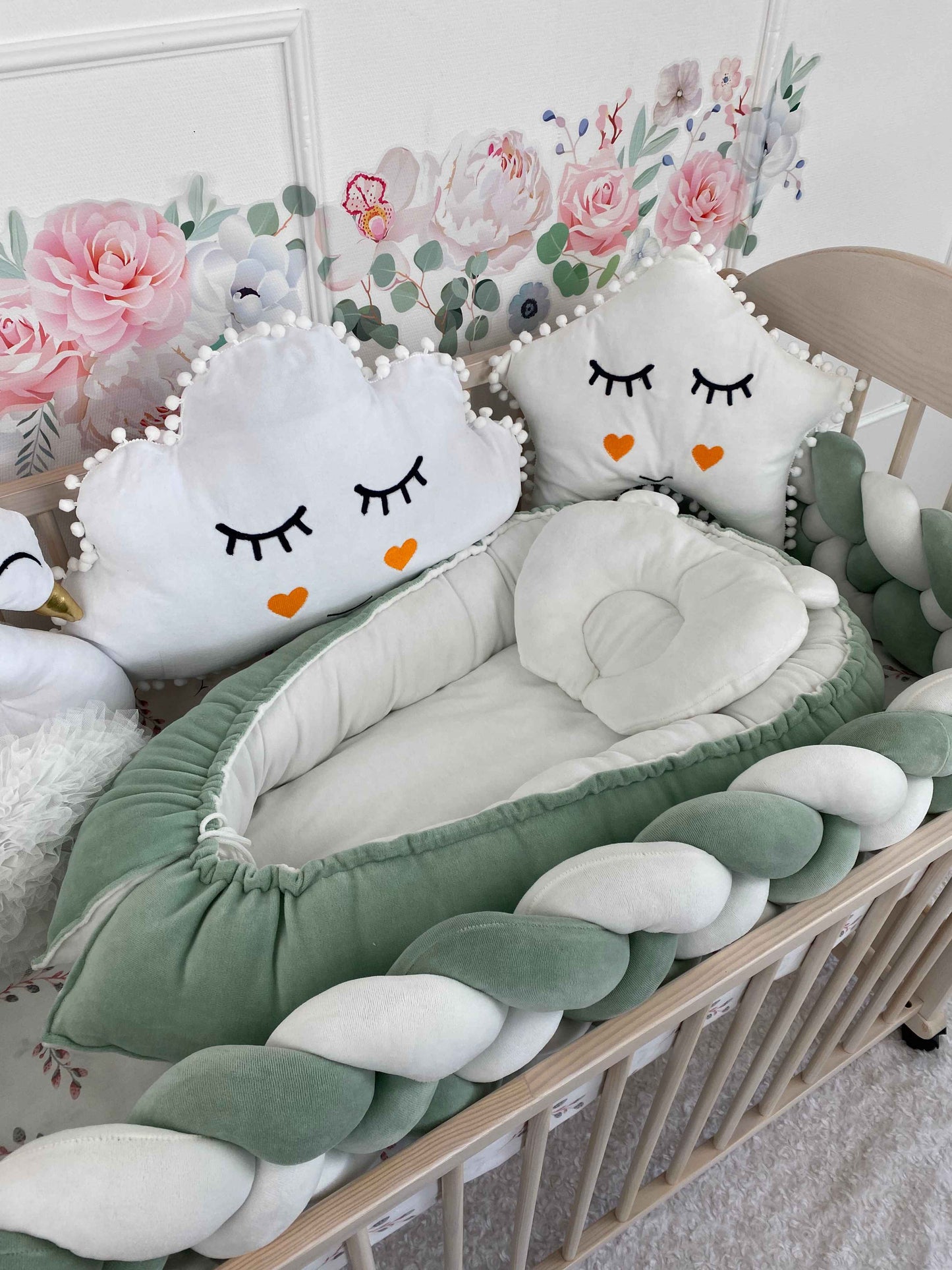 Green baby nest, braided bumper and white plush pillows in the crib. Natural materials.