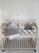 4-strip braided cot bumper, 3 free pillows and blanket on crib against white wall. Front side