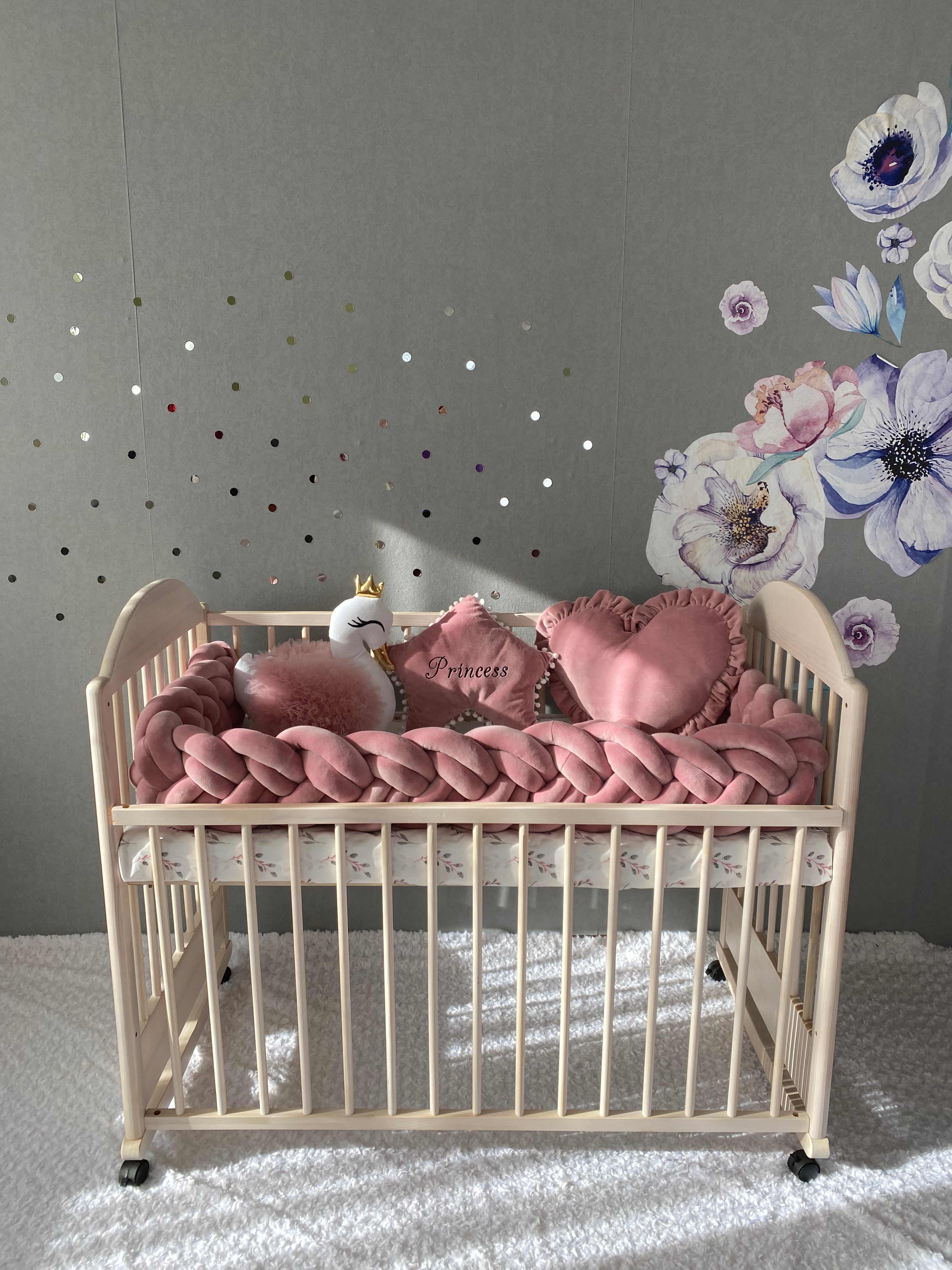 Double braided crib bumper, star, swan and heart pillows on the cot. Rose color. Front side.