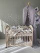 Crib set in light gray color. Braided Crib Bumper - Weaving in 4 Strips, star, cloud, swan pillows and blanket on the crib. Behind the bed on the right is a light grey canopy.