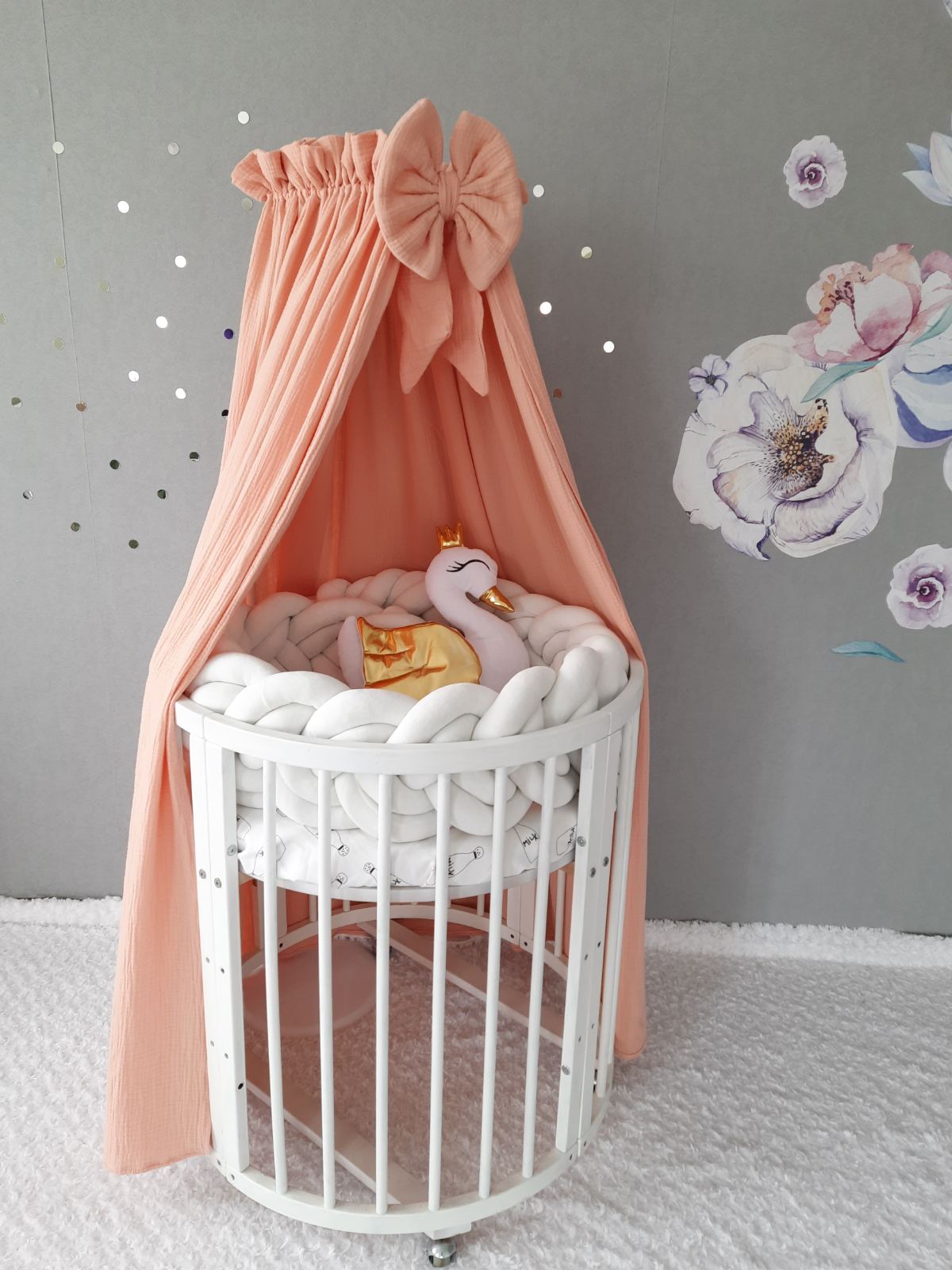 Muslin canopy in peach color for crib. White double braided cot bumper and swan pillow on the crib. Canopy over the bed.