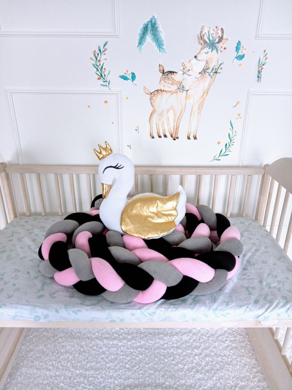 Triple Weaving Bumper on the crib in pink, gray and black colors with a white swan pillow on top of the braided bumper. Front side