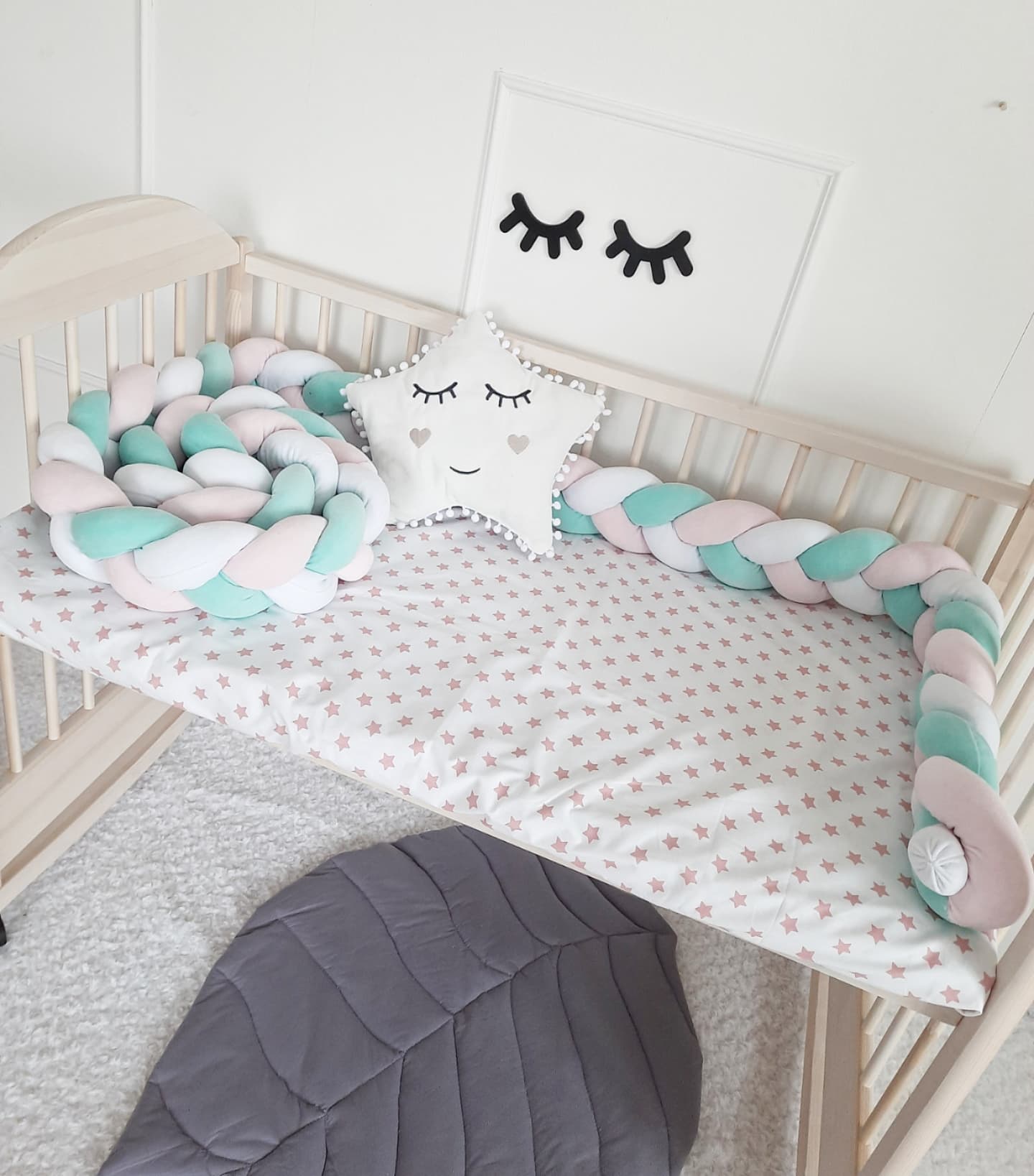 Triple Weaving Braided Crib Bumper in white, mint and light pink colors with white star pillow on crib. Front side view slightly right from the top